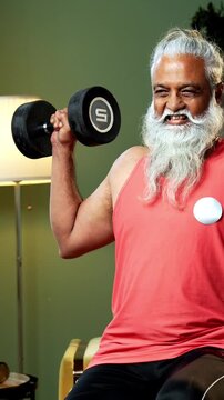 Indian mid age stylish bearded man doing exercise using dumbbell at home, fitness conscious mature male performing weight training workout showing strength, agility determination in modern interior