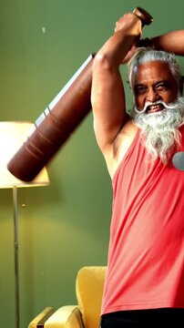 Indian mid age stylish bearded man doing exercise using mudgal or mudgar at home, handsome fitness conscious male performing traditional wooden strength training workout in modern interior