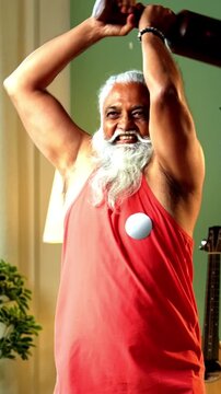 Indian mid age stylish bearded man doing exercise using mudgal or mudgar at home, handsome fitness conscious male performing traditional wooden strength training workout in modern interior