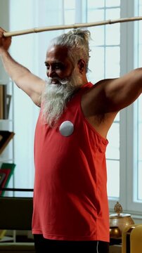 Indian mid age stylish bearded man doing exercise using stick, rod or staff at home, fitness conscious mature male performing strength and mobility workout showing agility and determination