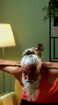 Indian mid age stylish bearded man doing exercise using stick, rod or staff at home, fitness conscious mature male performing strength and mobility workout showing agility and determination