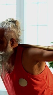 Indian mid age stylish bearded man doing exercise using stick, rod or staff at home, fitness conscious mature male performing strength and mobility workout showing agility and determination
