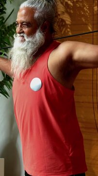Indian mid age stylish bearded man doing exercise using resistance band at home, fitness conscious mature male showing strength, agility and determination during workout in modern interior