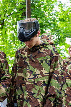 young man plays paintball, dressed in camouflage overalls and protective paintball mask in a forest area, DPM coloring, portrait of  guy in overalls