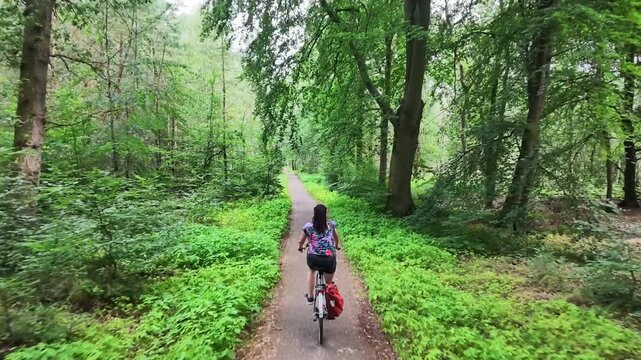 Woman cycling through a green woodland in summer
