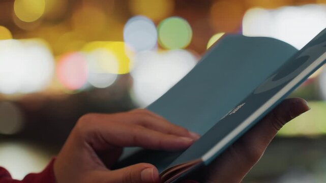 Walking at night with pages turning smoothly. Strolling through city with books during nighttime hours. Walking alongside illuminated streets while flipping through pages of book at night