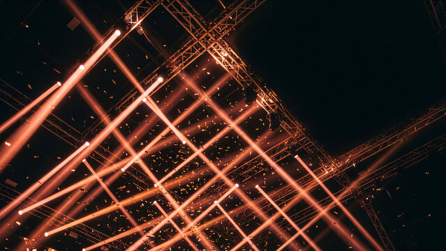 Stage lighting beams and confetti falling from a metal truss structure during a concert or event