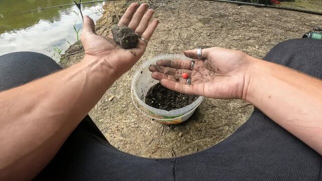 POV Close up of fisherman hands pressing groundbait mix around a method feeder with a hookbait. Carp (Cyprinus carpio) fishing preparation.