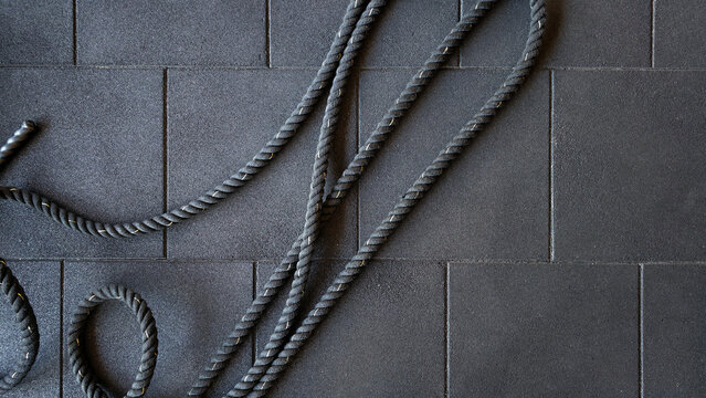 Battle ropes resting on black rubber gym flooring, symbolizing a dedication to fitness, athletic performance, and vigorous physical activity in a modern workout environment