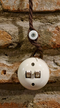Vintage ceramic light switch with braided cloth electrical wire on an exposed old brick wall, representing retro design, classic electricity, and rustic industrial decor
