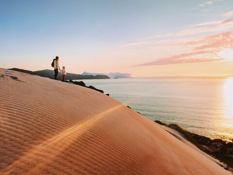 Family travel vacations mother and child on hiking trip enjoying sunset sea view standing on the top of sandy mountain, parent and kid explore northern Norway outdoors together active adventure tour