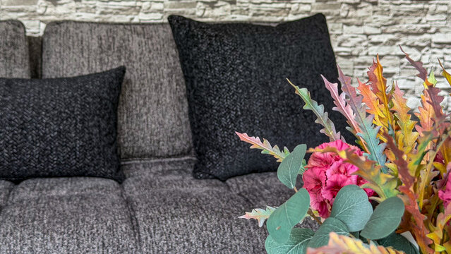 Decorative colorful flower arrangement in a modern gray living room interior with sofa, black cushions and textured stone wall. Contemporary home decor and cozy interior styling.