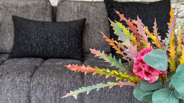 Decorative colorful flower arrangement in a modern gray living room interior with sofa, black cushions and textured stone wall. Contemporary home decor and cozy interior styling.