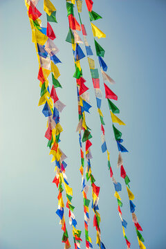 Colorful Buddhist prayer flags waving in wind against blue sky with copy space