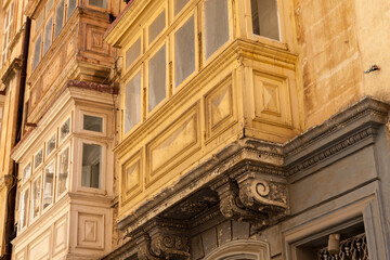 Weathered wooden gallarija balconies in a traditional colour palette overhang a baroque stone doorway in Valletta, Malta © Tony Blood