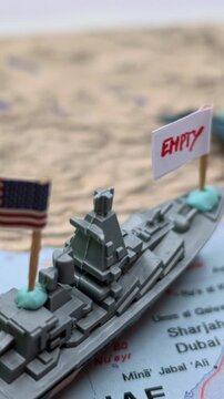 Conceptual representation of the US army facing an ammunition and weapon shortage crisis, with toy military vehicles on a map of Iran and the Strait of Hormuz showing empty flags