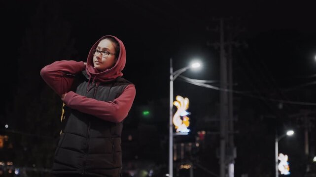 Urban night commuter. Nighttime pedestrian adjusting backpack. City streetwalker pauses near bright streetlamp. Evening traveler stops beside illuminated lamppost while adjusting gear