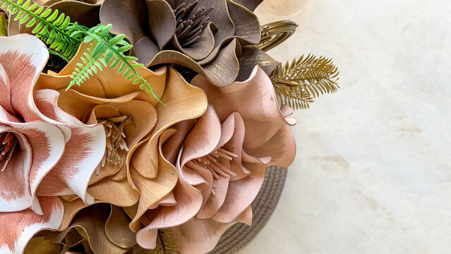 Close-up of elegant artificial floral arrangement in soft pink, beige, brown and gold tones on a light marble surface with copy space. Decorative flowers for modern home interior styling.