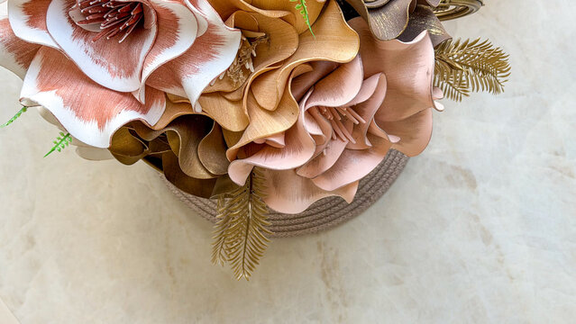 Close-up of elegant artificial floral arrangement in soft pink, beige, brown and gold tones on a light marble surface with copy space. Decorative flowers for modern home interior styling.