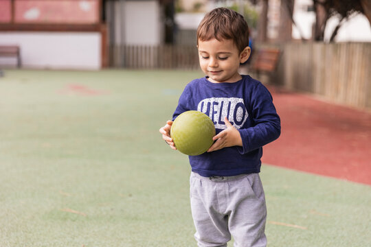Toddler boy playing ball on playground surface