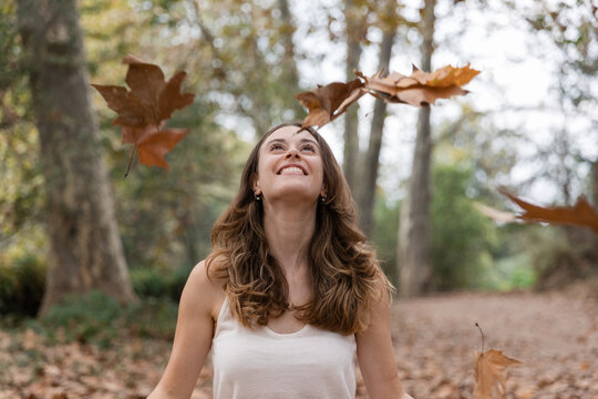Happy woman enjoying falling autumn leaves in forest