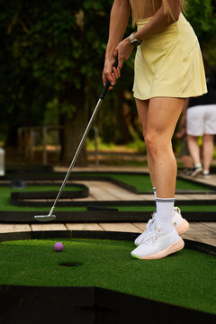 Girl holding a metal putter to hit a bright pink ball during an outdoor mini golf game