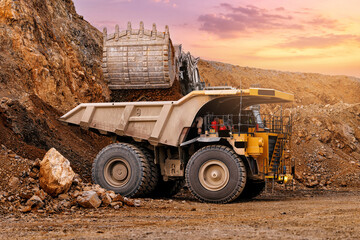 Giant mining dump truck being loaded by excavator at sunset in gold open pit for industrial transport background and heavy equipment © Parilov