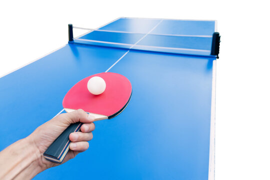 Hand holding a red ping pong paddle with ball balanced on it, poised above a blue tennis table isolated on white. Sport concept.