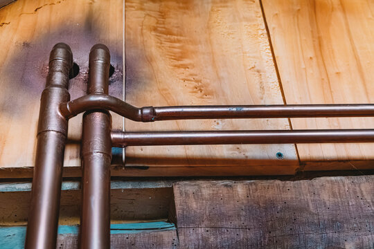 Warm-toned copper plumbing pipes branching along a rustic wooden wall inside a residential home, showcasing skilled craftsmanship.