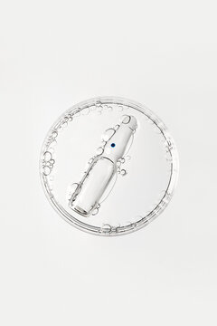 Transparent glass ampoule floating in liquid with bubbles in petri dish