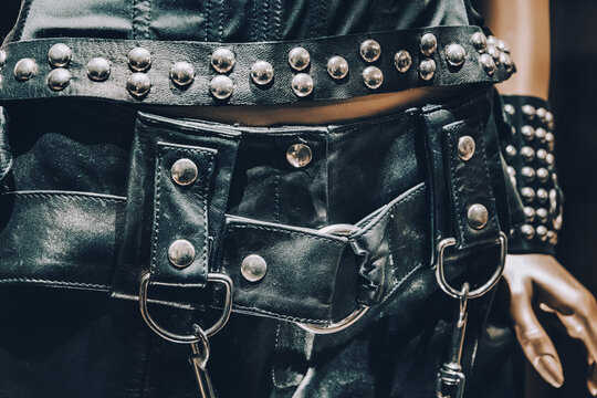 Mannequin showcasing rock fashion with studded leather clothing, wristbands, and a chain accessory against a wooden background