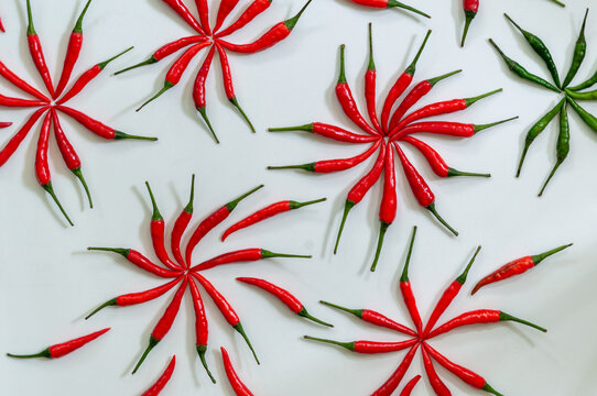 Creative flat lay of red chili peppers arranged into pinwheel shapes on a white background. Playful geometric food composition with green chili creating contrast, perfect menus and modern design.