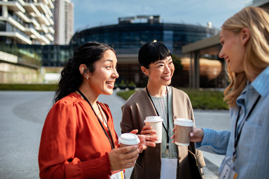 Three businesswomen networking with coffee outside a modern office