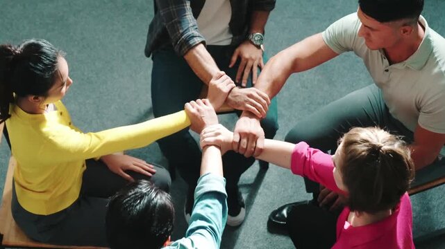 Top down aerial view of diverse business people hold wrist while sitting circle together. Faithful prayers holding wrist or hand of each other. Represented teamwork, unity, togetherness. Symposium.