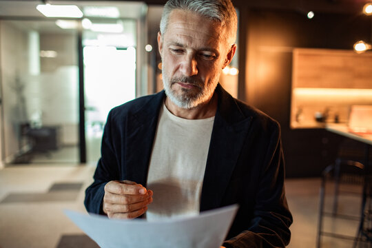 Thoughtful senior businessman reviewing document in modern office