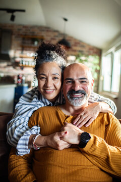 Smiling mature couple hugging on couch at home