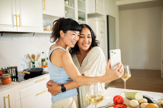 Two women taking a selfie while cooking together in a bright home kitchen