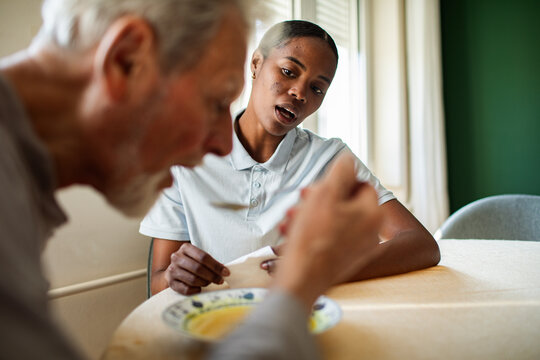 Caregiver helping senior man eat soup at home
