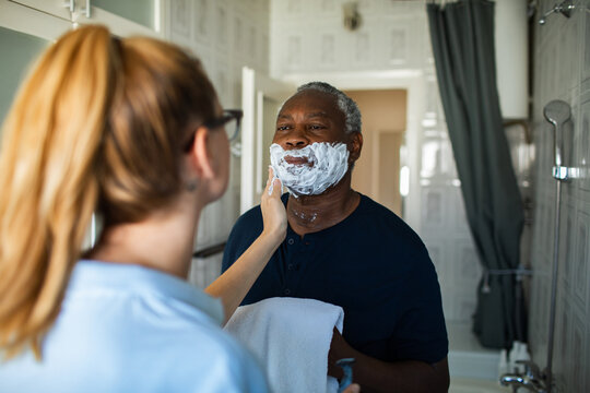 Caregiver helping senior man shave in home bathroom