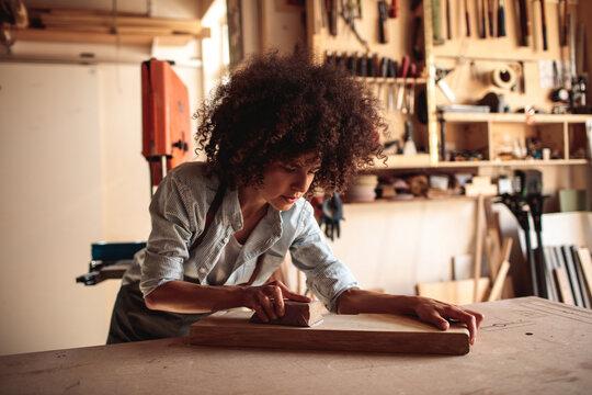 Woman sanding wooden board in carpentry workshop