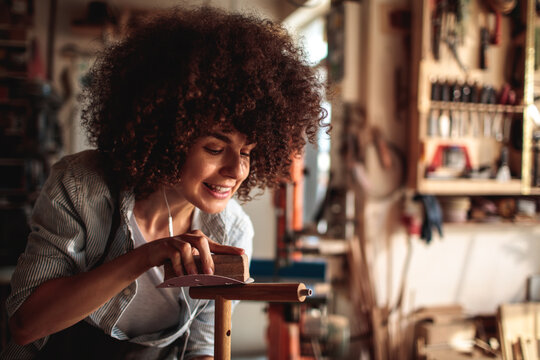 Smiling woman sanding wood in home workshop