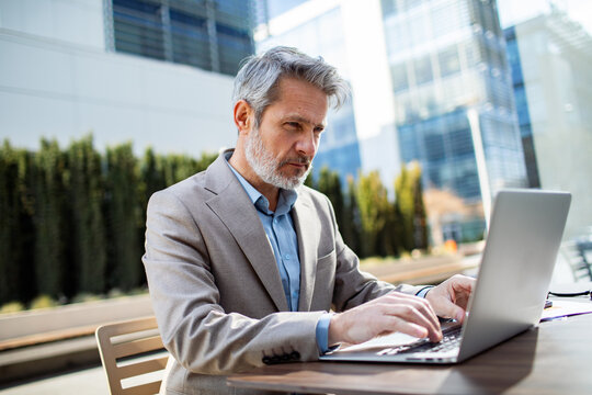 Mature businessman working on laptop outdoors in urban office district