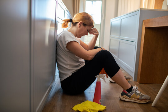 Tired woman sitting on kitchen floor after cleaning