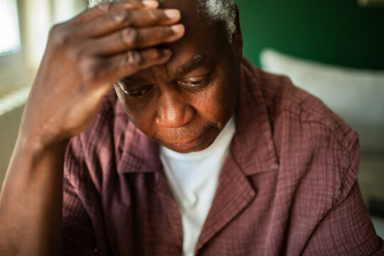 Worried senior man holding forehead at home