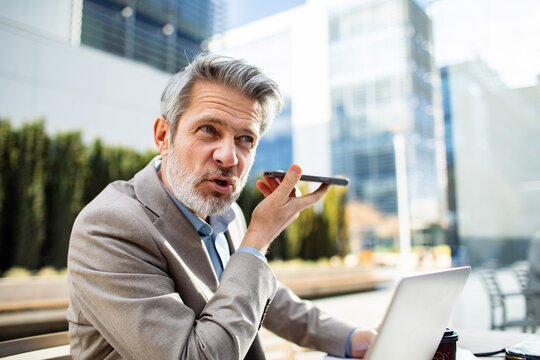 Senior businessman dictating on smartphone at outdoor office courtyard