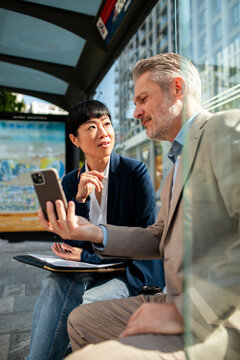 Two business colleagues using smartphone at city bus stop