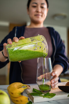 Woman pouring green smoothie into glass in home kitchen