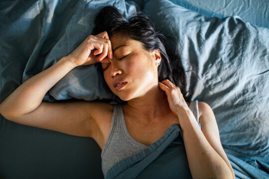 Tired woman with headache resting in bed at home