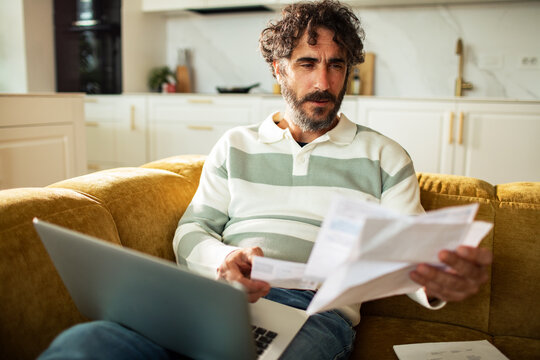 Middle-aged man reviewing household bills on laptop at home