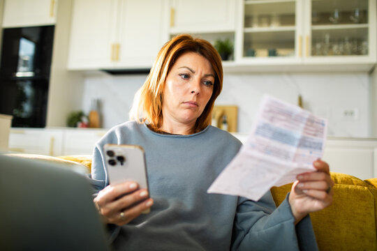 Concerned woman reviewing household bills with smartphone at home